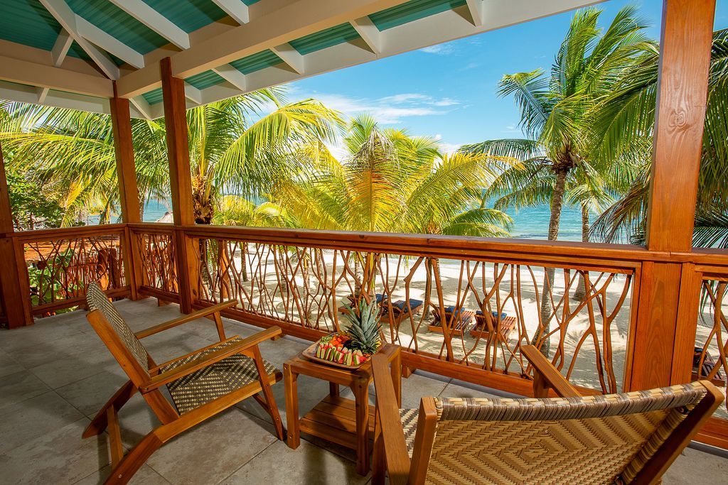 Beachfront porch with woven chairs, wooden railing, and palm trees overlooking turquoise water