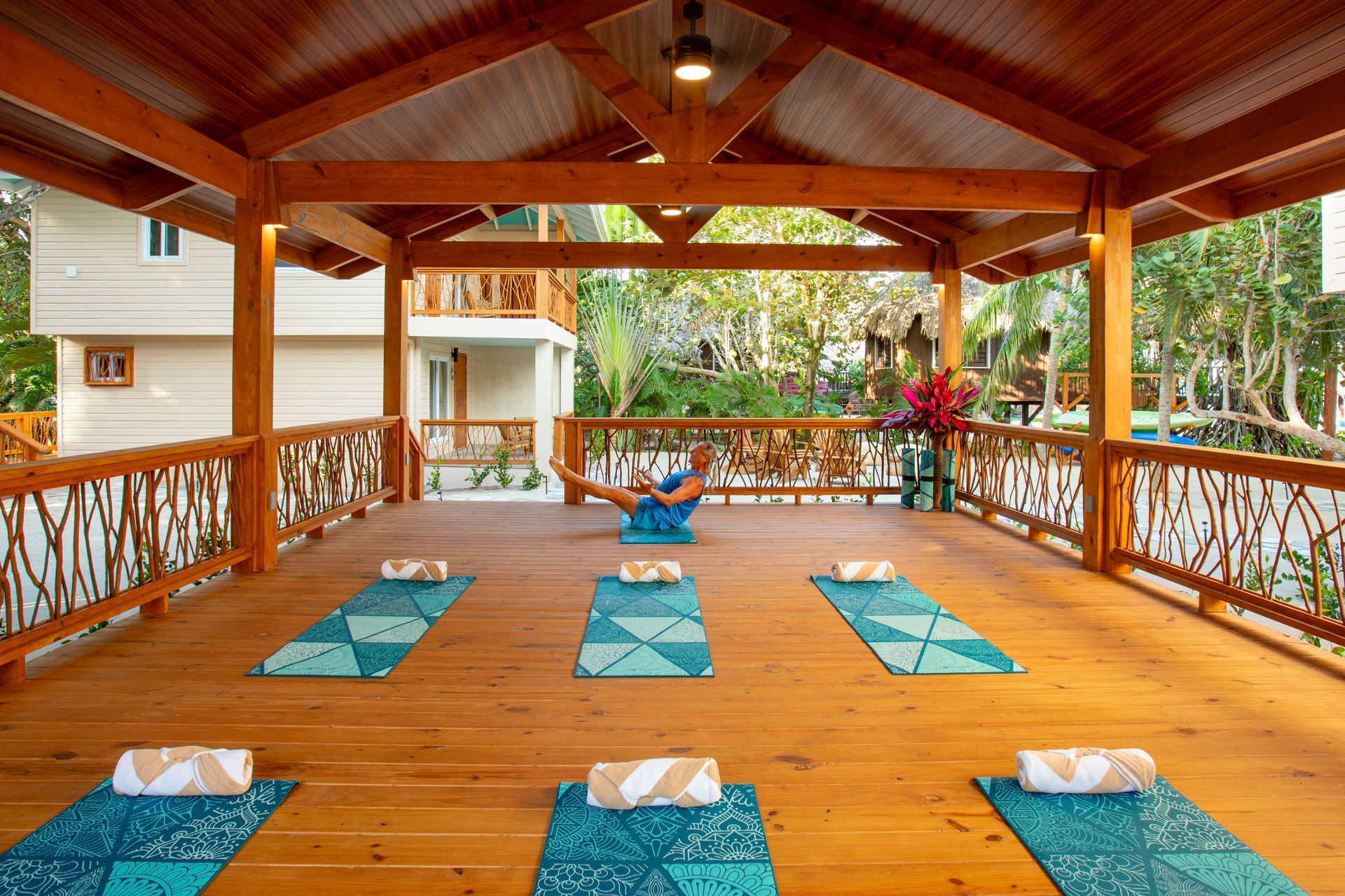 Wooden yoga pavilion with turquoise mats arranged in rows under a covered roof, surrounded by greenery