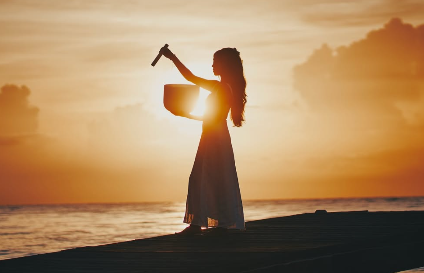 Silhouetted person playing violin at sunset on a beach