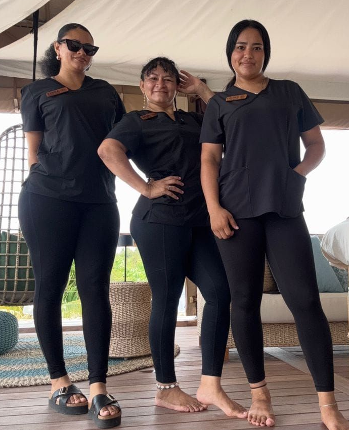 Three people in black outfits and sunglasses standing barefoot under a canopy.