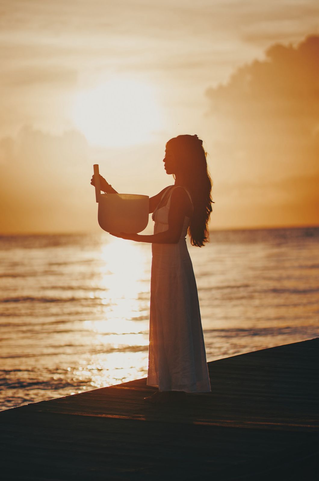 Silhouette of a person in a white dress holding up a bottle at sunset by the sea