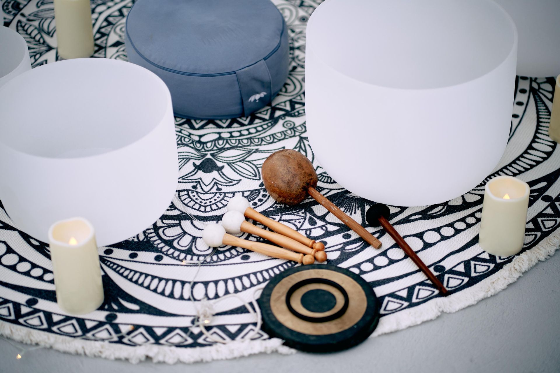 Meditation set with singing bowls, mallets, candles, and cushions on a patterned mat