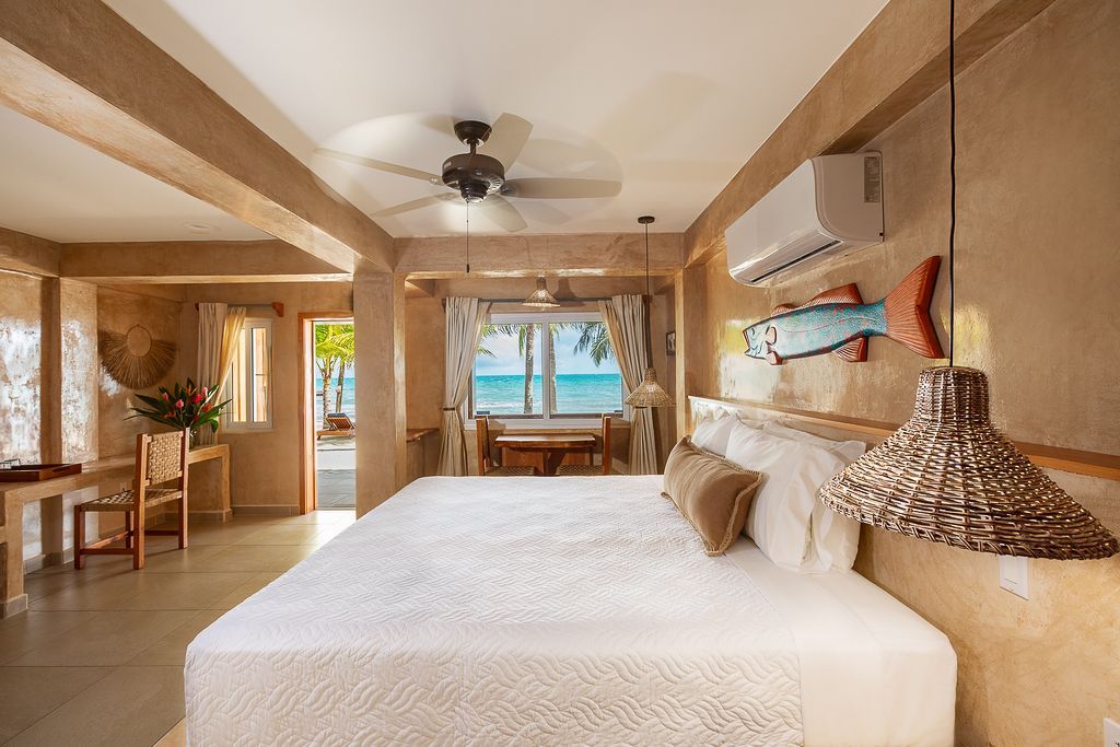 Bright beachside bedroom with a king bed, wooden decor, and ocean view through open doors