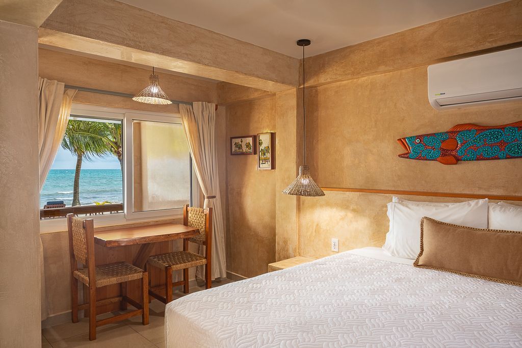 Cozy hotel room with a bed, desk by a window, and a view of palm trees and the ocean