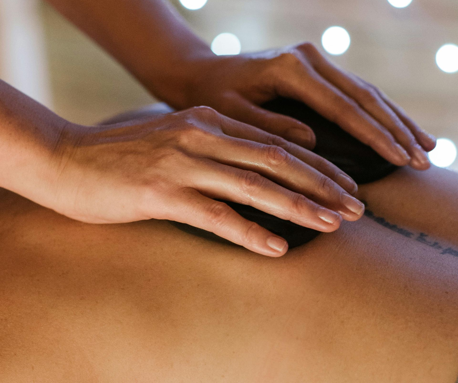 Hands gently massaging a person's bare back in a soft, spa-like setting with blurred lights