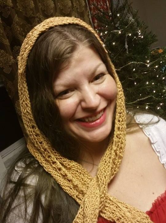 A woman wearing a scarf around her head smiles in front of a christmas tree