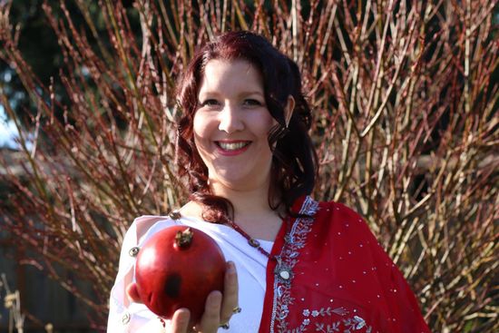 A woman in a red and white dress is holding a pomegranate.