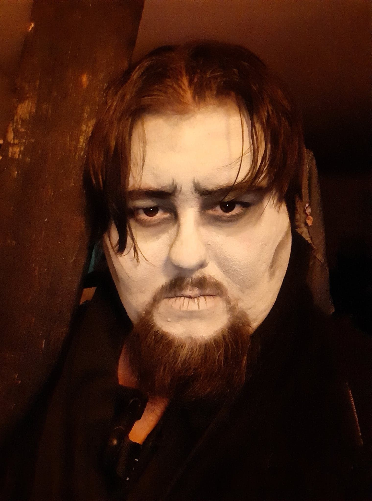 A man with a beard and white paint on his face is looking at the camera, Nikodaemus Shadowsky representing Hades.