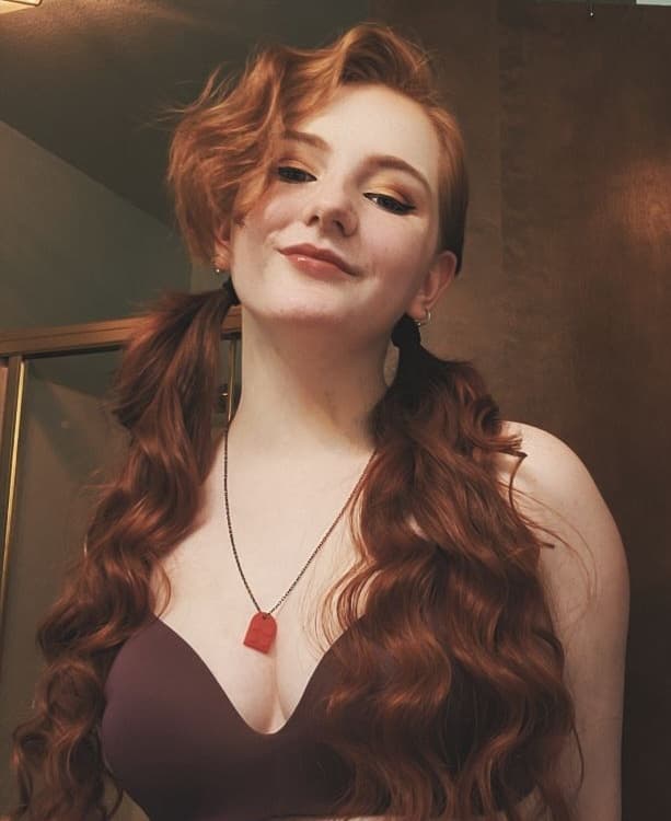 A woman with red hair is wearing a bra and a necklace