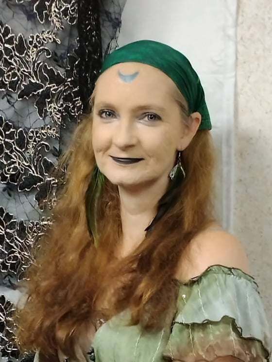 A woman with long red hair is wearing a green headband and earrings, Ivy Moon