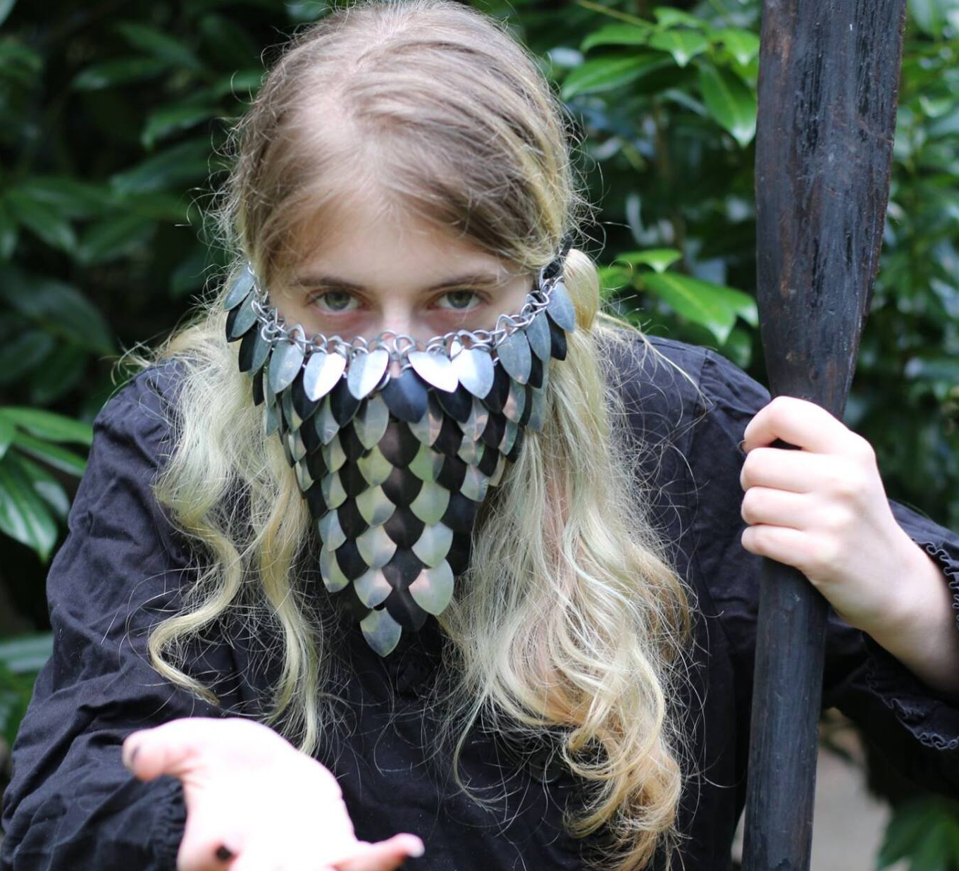A woman with a mask on her face is holding a stick, Rebecca Delph representing Charon.