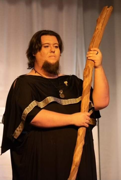 A man with a beard is holding a long wooden stick, Nikodaemus Shadowsky