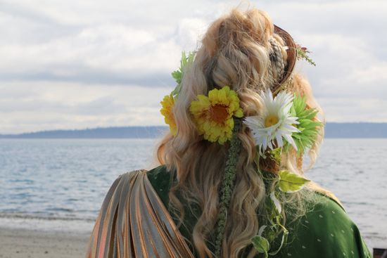 A woman with flowers in her hair is standing on a beach looking at the ocean.
