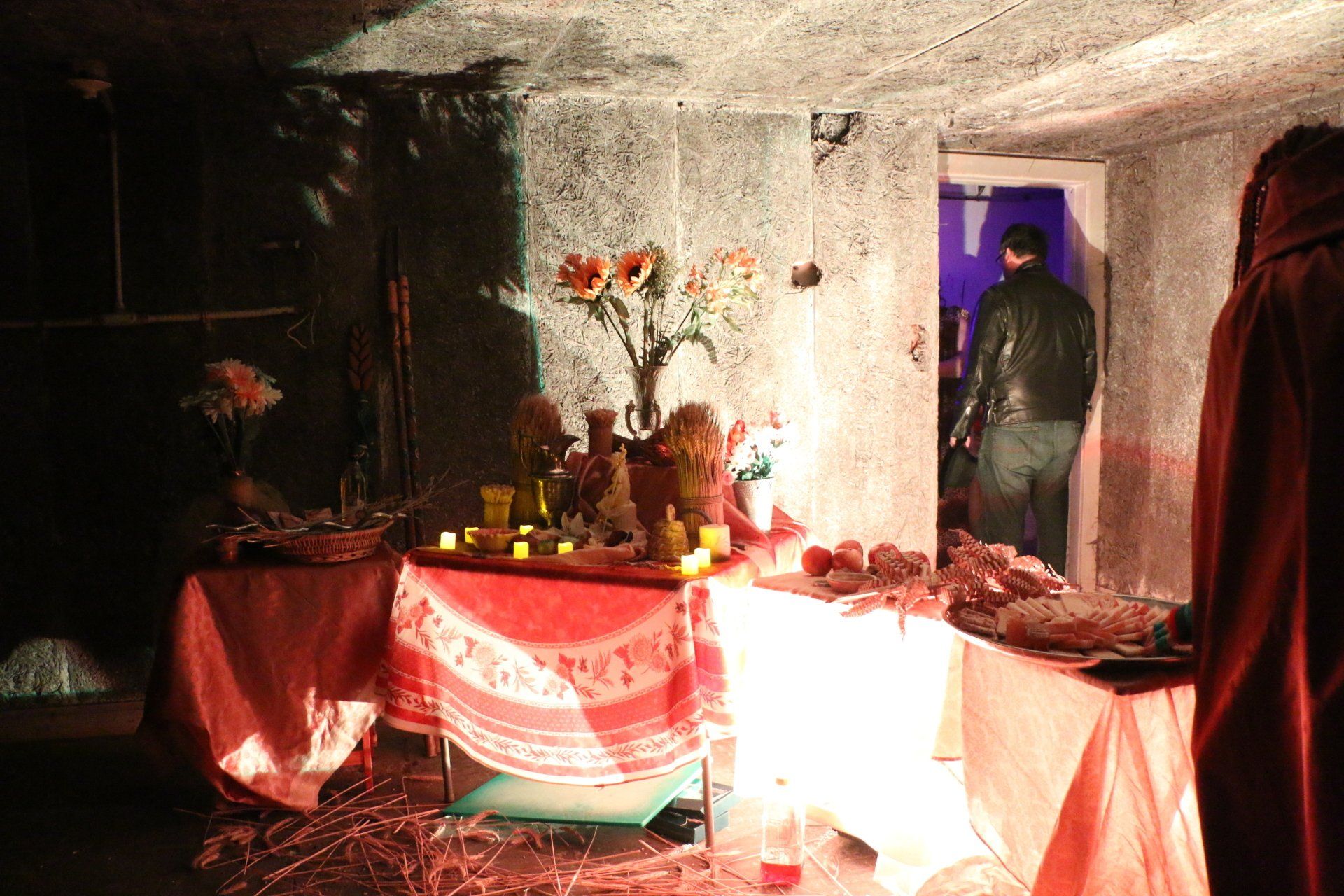 A man in a black jacket is standing in a dark room behind a table with candles on it.