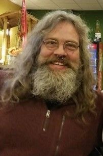 A man with long hair and a beard is smiling for the camera, Michael Alling.