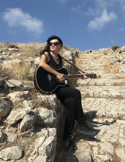 A woman is sitting on a rock holding a guitar.