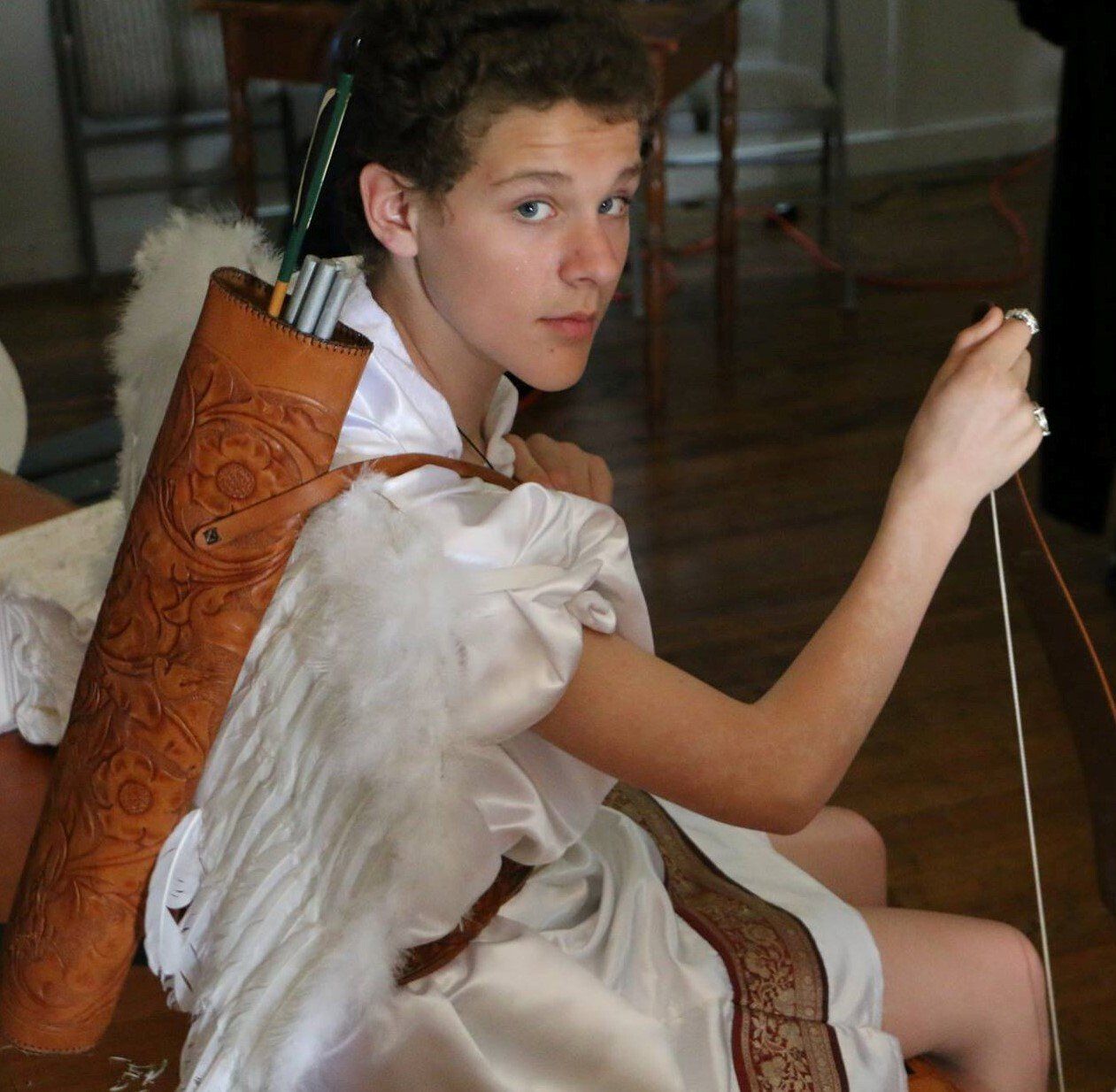 Person wearing white and wings, with arrows, representing Cupid.