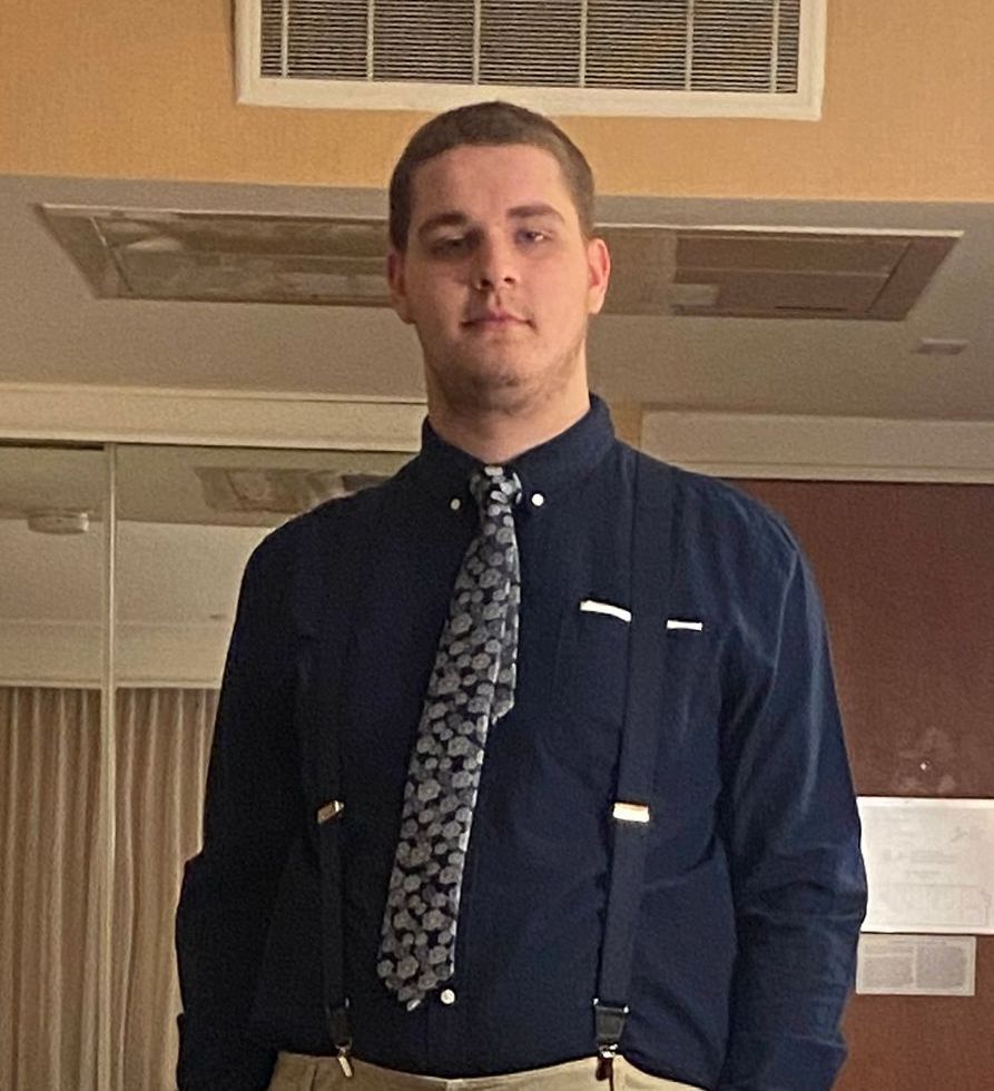 A man wearing suspenders and a tie stands in a room, Victor Malinski.