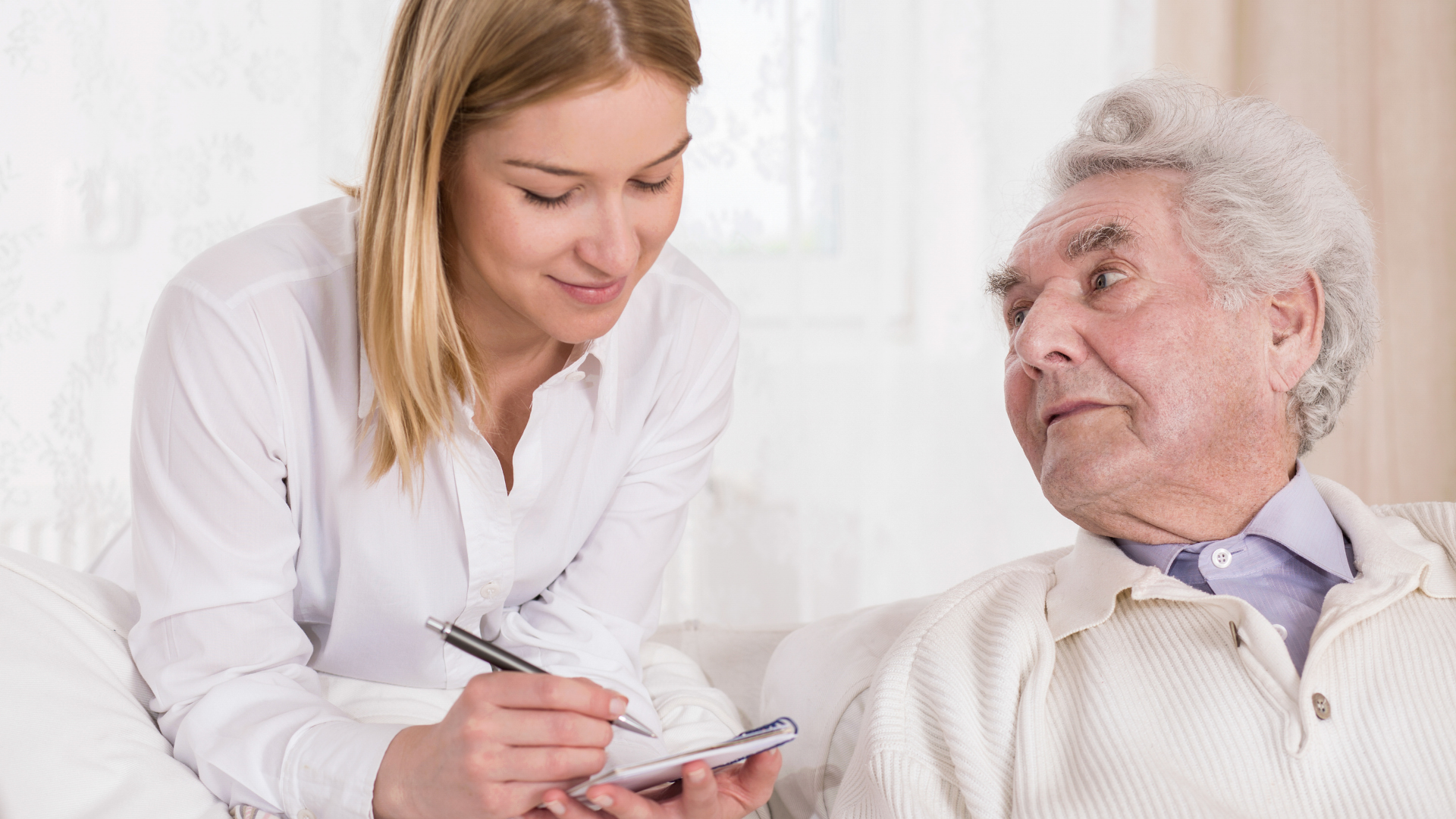 Woman in white shirt, assisting an older man with writing, indoors.