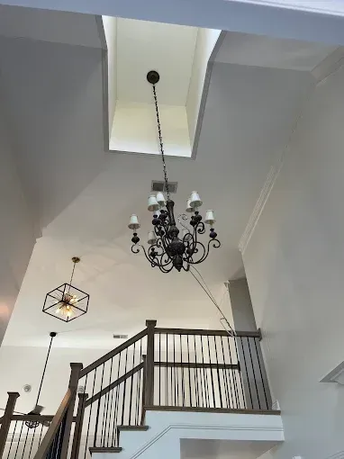 High-ceilinged foyer with a chandelier, skylight, and staircase. White walls, dark fixtures, wood banister.