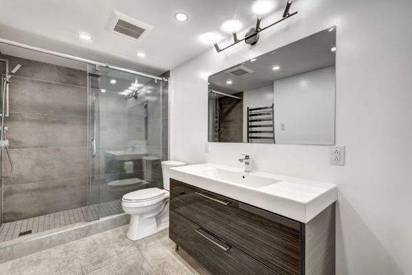 Modern bathroom with a glass shower, gray tiles, and a dark wood vanity.