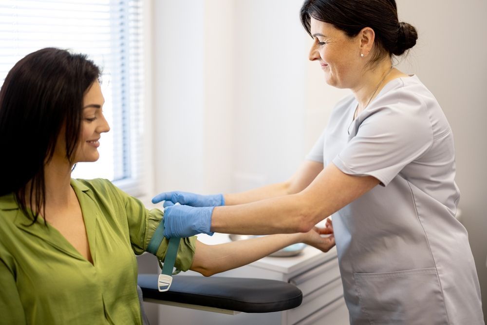 Nurse in scrubs draws blood from seated patient in a clinic, using a tourniquet and gloves