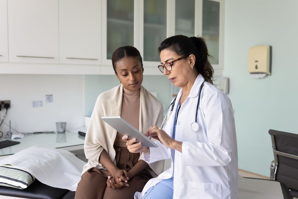 Doctor reviewing tablet with seated patient in a bright clinic exam room