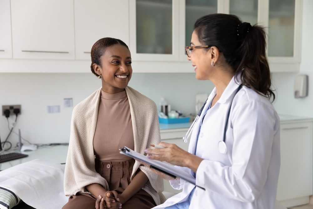 Doctor speaking with a smiling patient in a bright exam room.