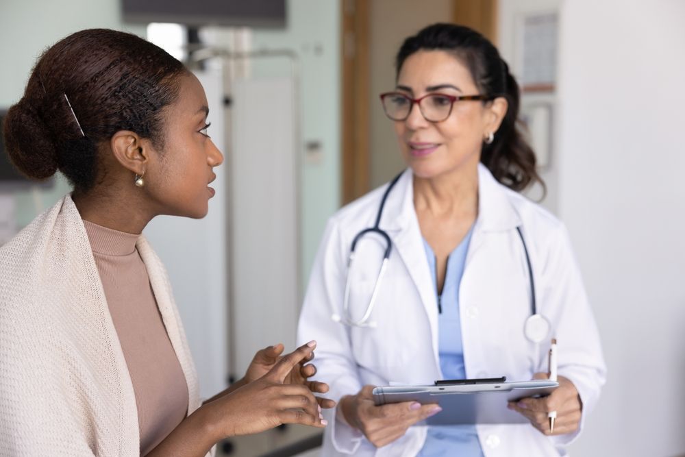 Woman talking to a doctor in a medical office. The doctor holds a clipboard and listens attentively.