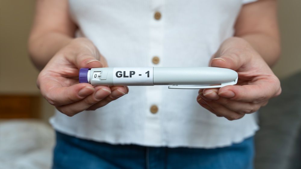 Hands holding a white GLP-1 injector pen against a blurred background.