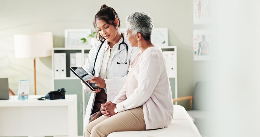 Doctor showing tablet to seated patient in a bright clinic room