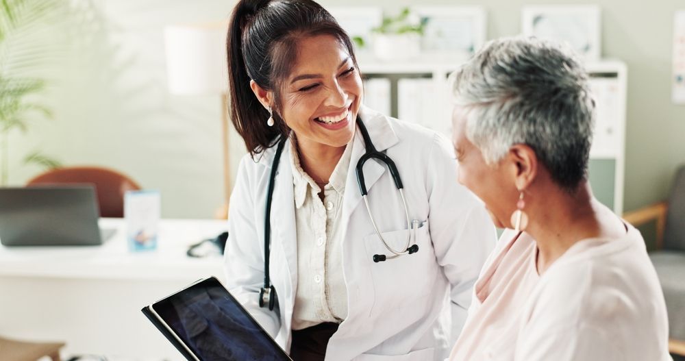 Smiling doctor with a stethoscope showing a tablet to a patient in a medical office.