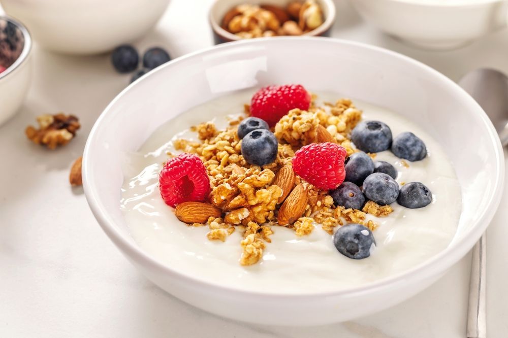 Bowl of yogurt topped with granola, raspberries, blueberries, and almonds.