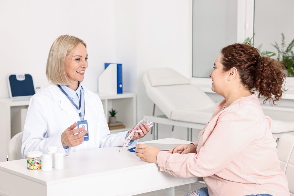 Doctor talking with a patient in a bright clinic office, holding papers across a desk.
