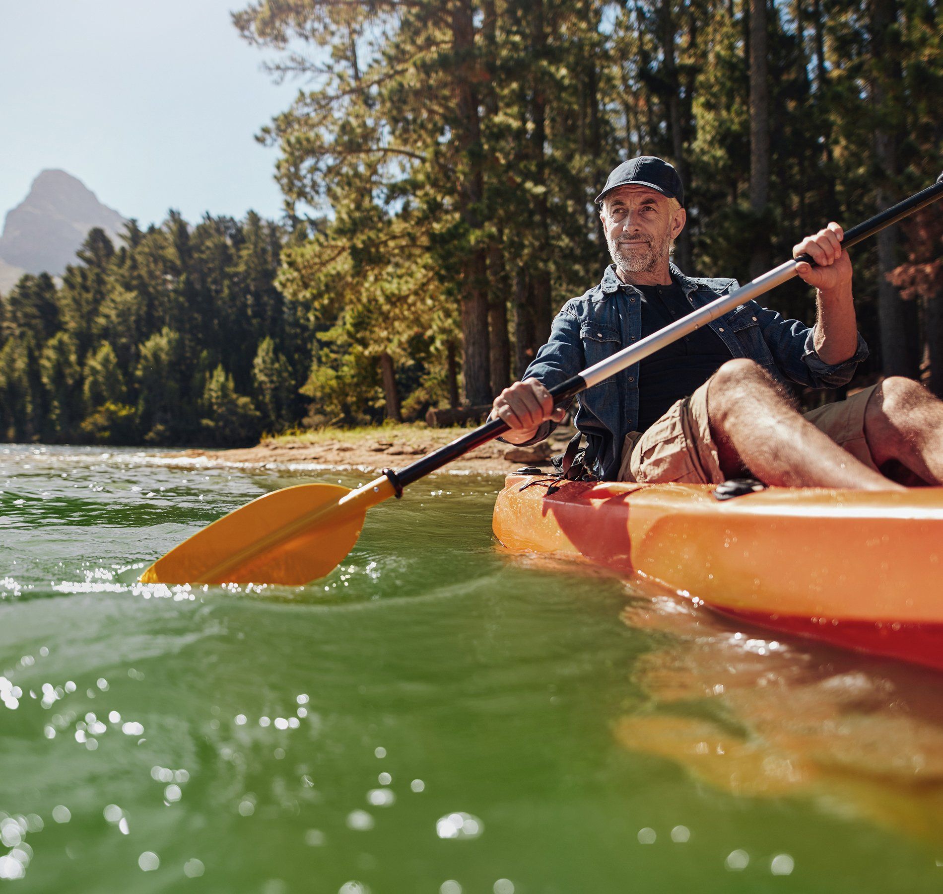 A man is paddling an orange kayak on a river.