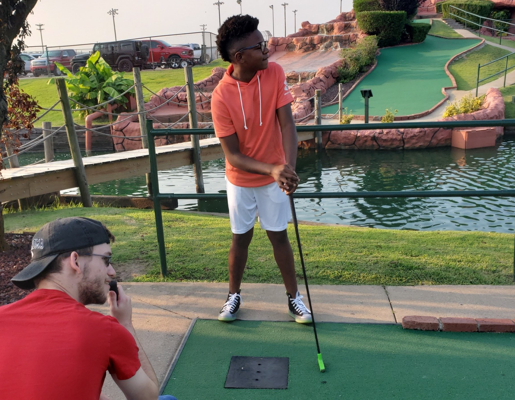 A young boy in an orange shirt is playing mini golf