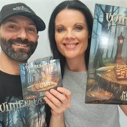 Twee lachende mensen houden fantasyboeken omhoog voor een achtergrond met een bos en lantaarns.