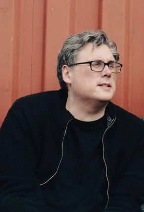 Gitarist in een zwart shirt die op een elektrische gitaar speelt op het podium onder groene lichten.