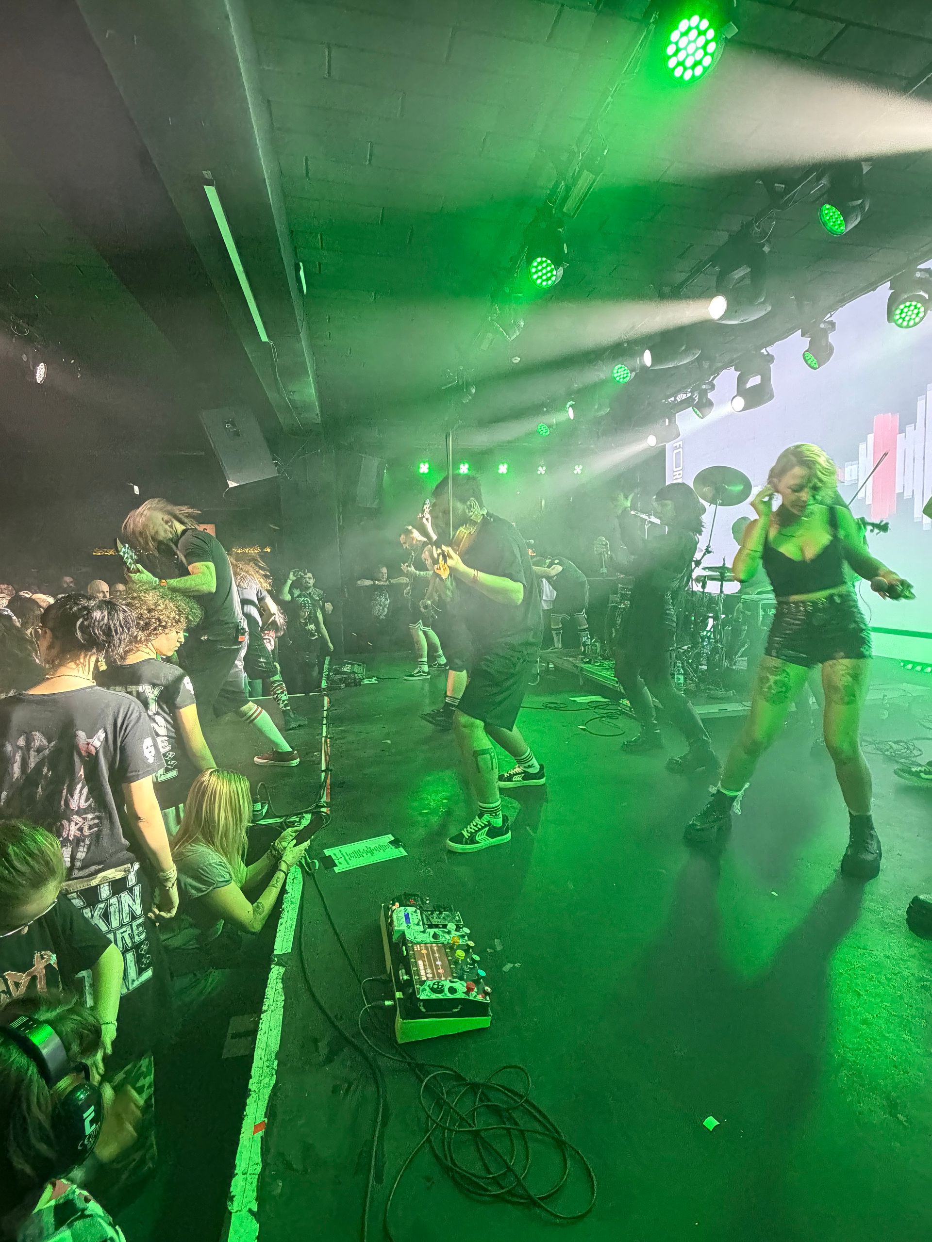 Een liveband treedt op op een groen verlicht podium met muzikanten en microfoons onder felle schijnwerpers.