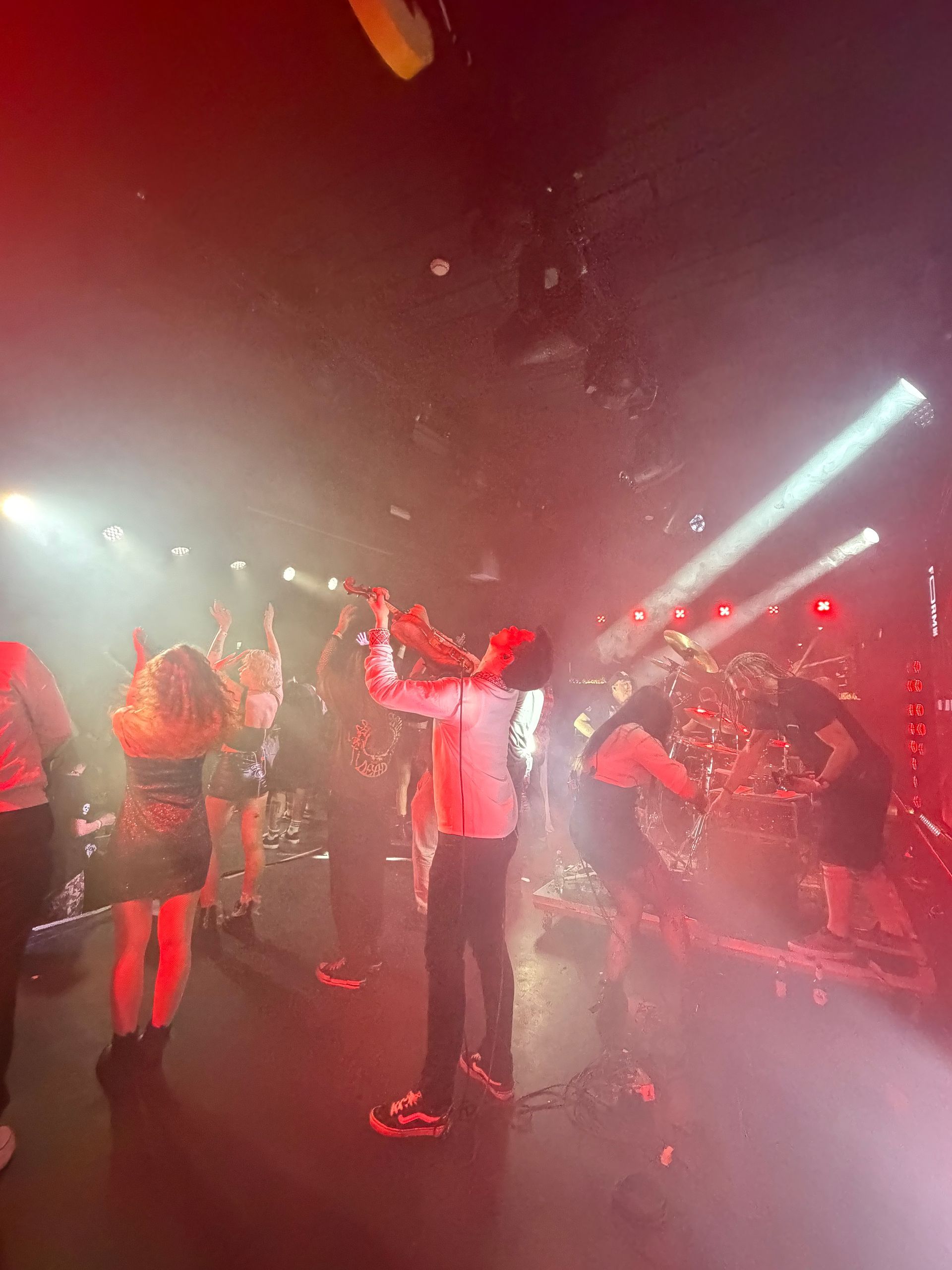 Mensen dansen in een rood verlichte club met mist en felle podiumverlichting.