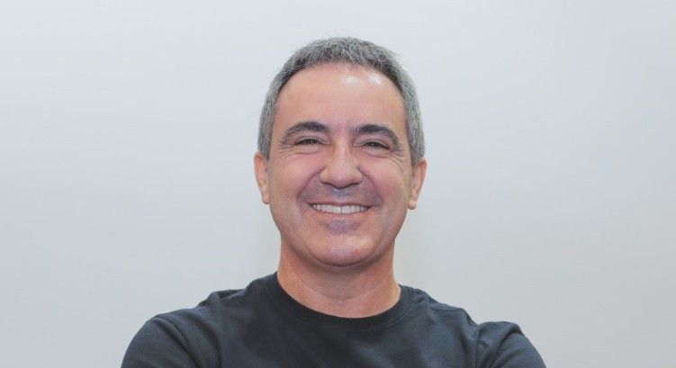 Um homem de camisa preta está sorrindo com os braços cruzados.