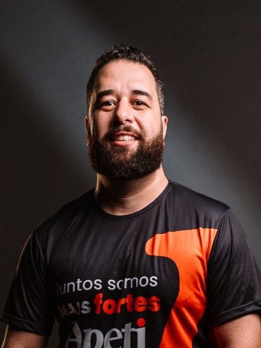 Um homem com uma jaqueta bege e camisa preta está parado em frente a uma janela.
