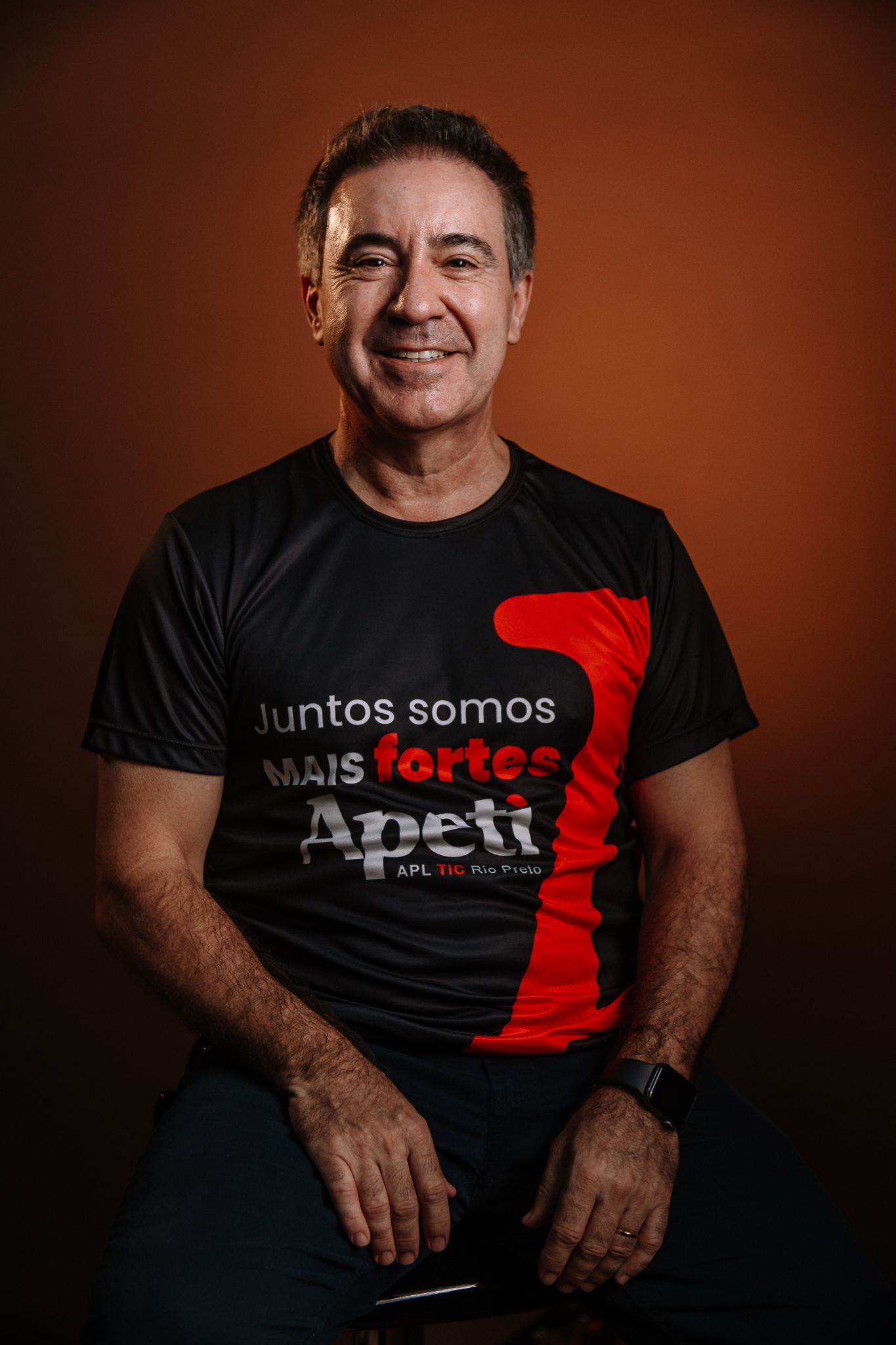 Um homem de camisa preta com os braços cruzados sorri para a câmera