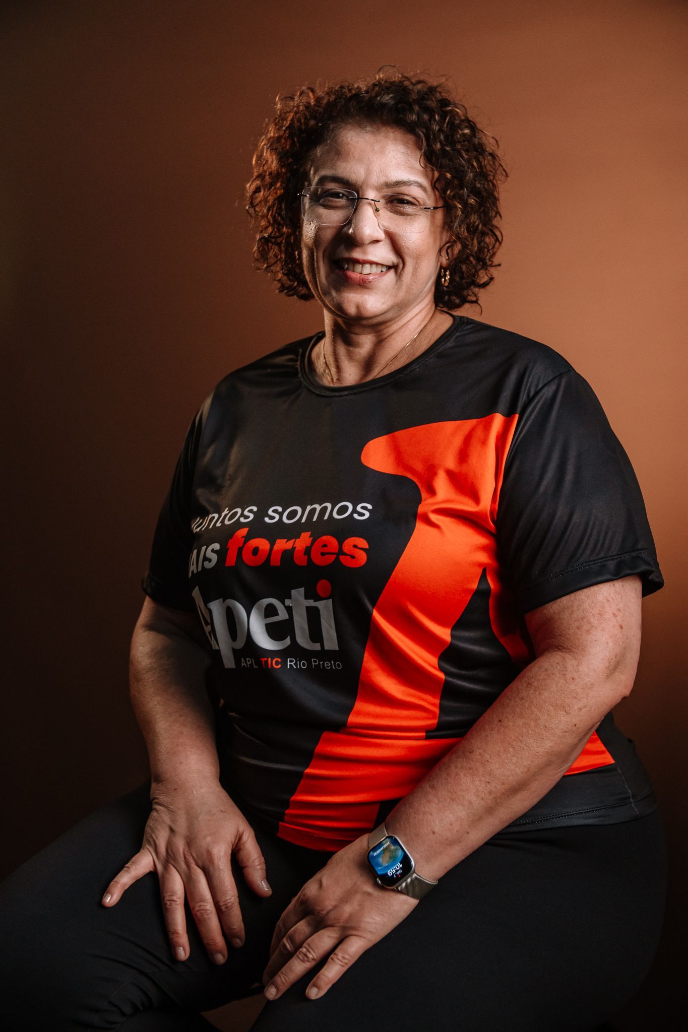 Uma mulher com cabelos cacheados e óculos está sorrindo para a câmera