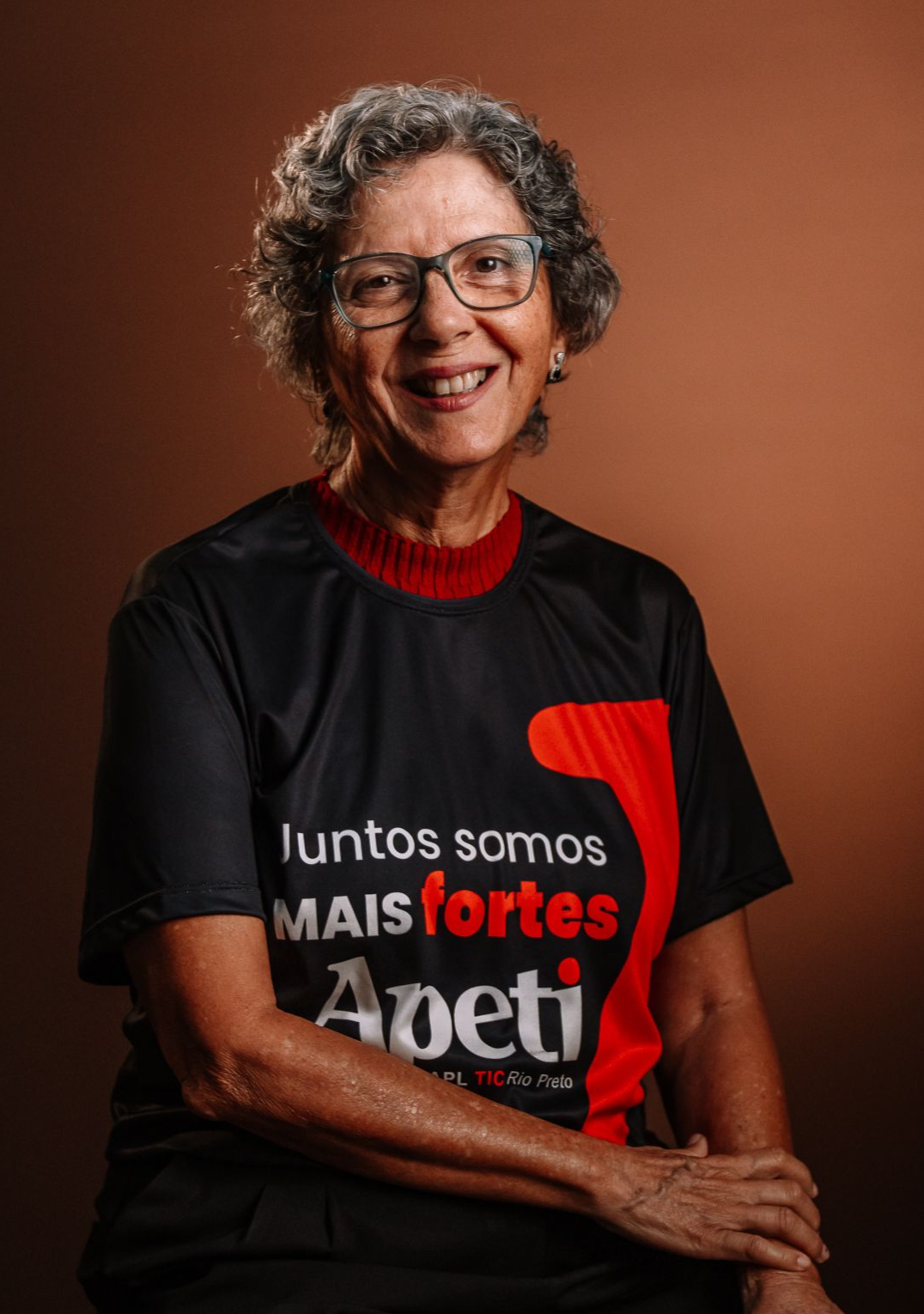 Uma mulher está sentada em uma cadeira vestindo uma jaqueta preta e um suéter verde.