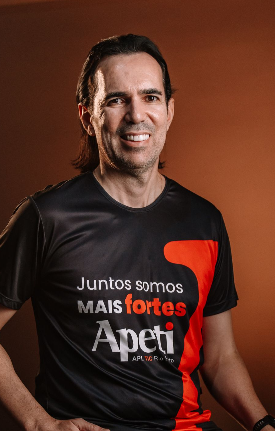 Um homem de camiseta cinza está de pé com os braços cruzados e sorrindo.