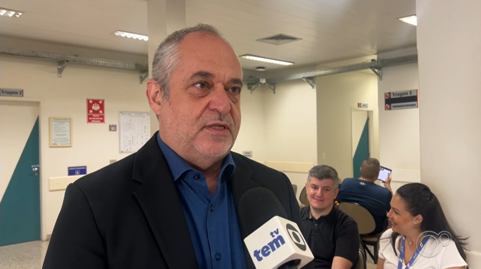 Um homem de terno está falando em um microfone em um hospital.
