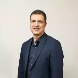 Um homem de terno e camisa preta está sorrindo para a câmera.