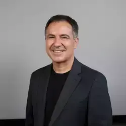 Um homem de terno e camisa preta está sorrindo para a câmera.