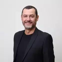 Um homem de terno preto e camisa preta está sorrindo para a câmera.